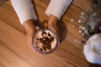 Hand holding hot aromatic cappuccino with foam and chocolate powder