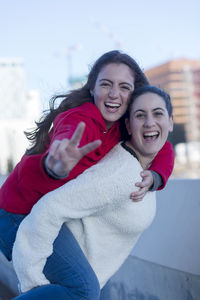 Happy female friends standing on building terrace against sky