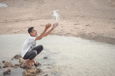 Side view of young man playing in water at beach