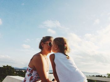 Mother and daughter face to face against sky