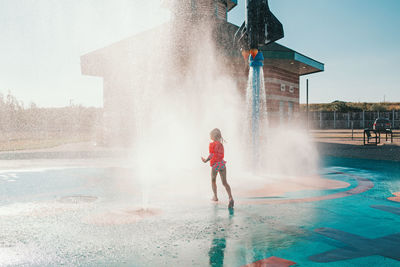 Cute adorable caucasian funny girl playing on splash pad playground on summer day. 