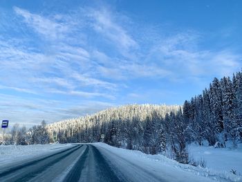 Road by snowcapped mountains against sky during winter