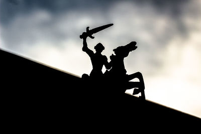 Silhouette men with arms outstretched against sky