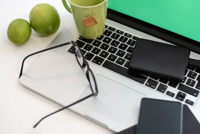 Laptop on table with green screen hot cup of tea and smartphone. accessories, devices for home work