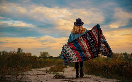 Rear view of woman standing on field against sky during sunset