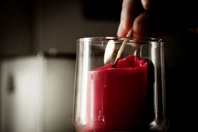 Fingers of man lighting a red candle inside a transparent glass vase with a match