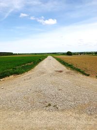 Empty road amidst field against sky