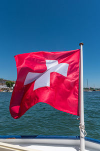 Portrait photo of the swiss flag fluttering in the wind from a boat on lake geneva.
