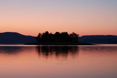 Silhouette trees by lake against romantic sky at sunset