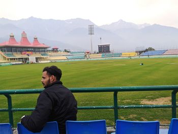 Man sitting on seat in field against mountains