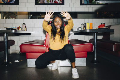 Cheerful woman gesturing while crouching against sofa in cafe