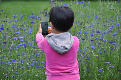 Rear view of girl photographing on field