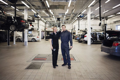 Portrait of happy experts standing arm around in auto repair shop