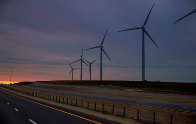 Wind turbines on field against sky during sunset