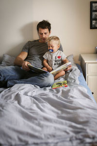 Man reading book with baby boy in bedroom