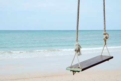 Empty swing at beach against sky