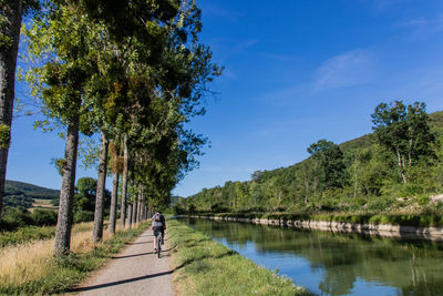 Rear view of woman riding bicycle by canal