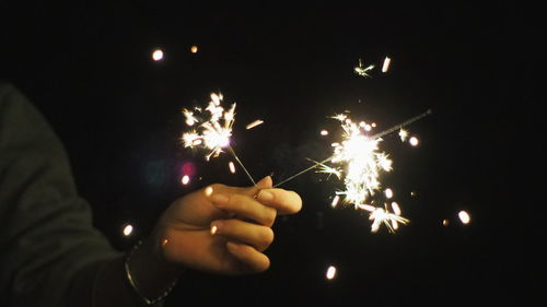 Cropped hand with burning sparkler at night