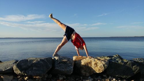 Man doing handstand at beach against sky