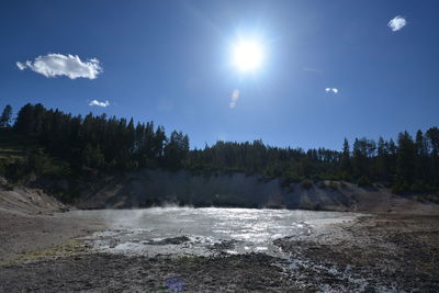 Scenic view of waterfall in forest against bright sun