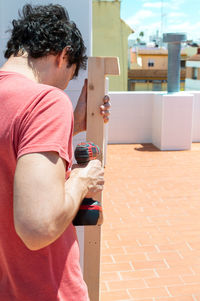 Man using a drill to build a shelf on a rooftop during a sunny day.