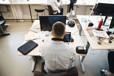 Rear view of male computer programmer using laptop on desk while sitting in creative office