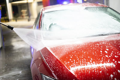 Person washing a red car with high pressure water in a car wash.