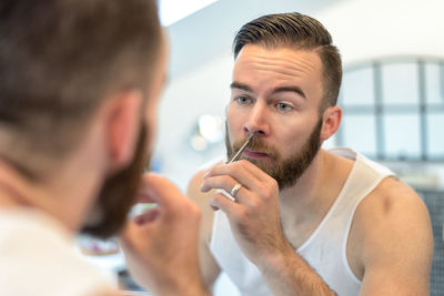 Close-up of young man cutting beard reflecting on mirror at home