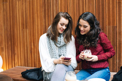 Smiling young woman using smart phone while sitting in mirror