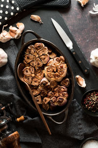 Freshly baked garlic bulbs in a roasting dish on a black slate board.