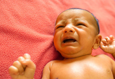 High angle view of shirtless baby boy crying while lying on bed