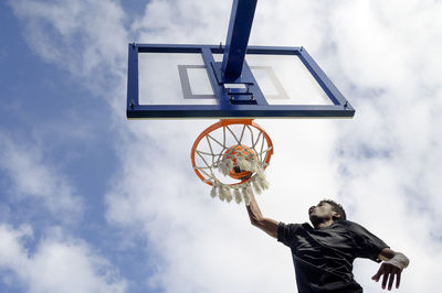 Low angle view of man holding basketball hoop against sky