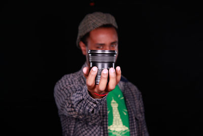 Close-up portrait of man holding lens against black background