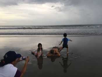 Rear view of friends photographing sea against sky