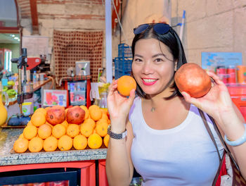 Portrait of smiling woman holding fruits while standing in market