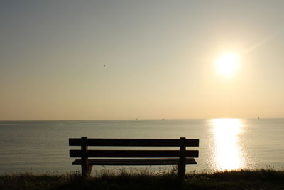 Bench on beach against sky during sunset