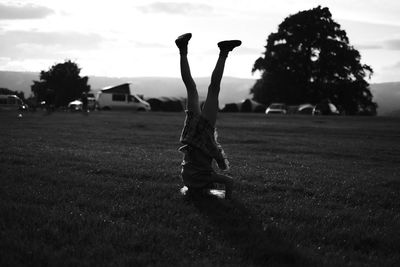 Woman practicing handstand on field against sky