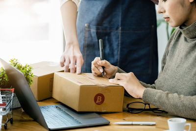 Woman writing on box while colleague pointing on it at shop