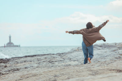 Rear view of woman standing at beach against sky