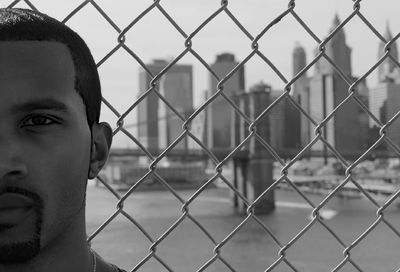 Portrait of man by chainlink fence against building