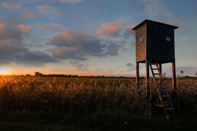 Lifeguard hut on field against sky during sunset