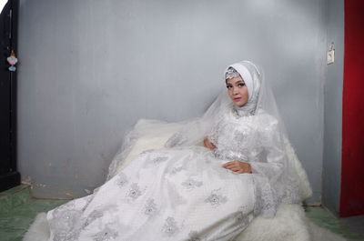 Portrait of bride wearing traditional clothing sitting against wall