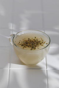 Healthy bone broth with spices in a mug on a white tile with a shadow pattern.