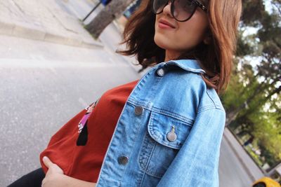 Tilt image of smiling young woman wearing denim jacket on road