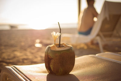 Close-up of coconut on lounge chair at beach during sunset
