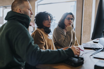 Multiracial female and male hackers discussing over computer at desk in startup company