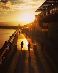 Silhouette people walking on bridge by sea against sky during sunset