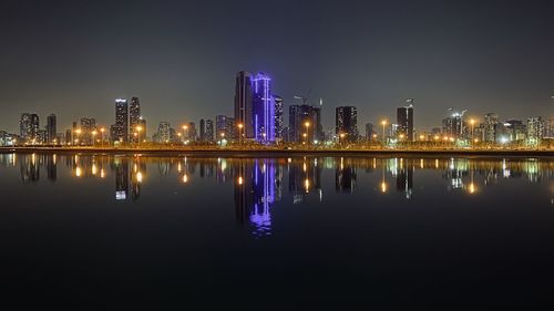 Illuminated buildings by river against sky at night