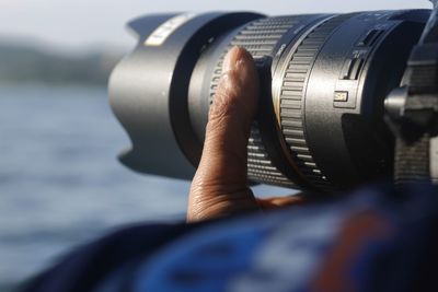 Cropped hand holding camera against lake