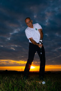 Man playing golf on field during sunset